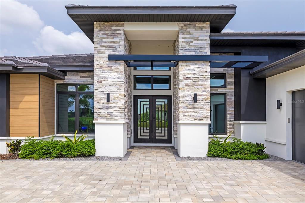 The exterior of a modern home features a stone-clad entryway with double glass doors — 4116 BUTTE TRAIL, BRADENTON, FL