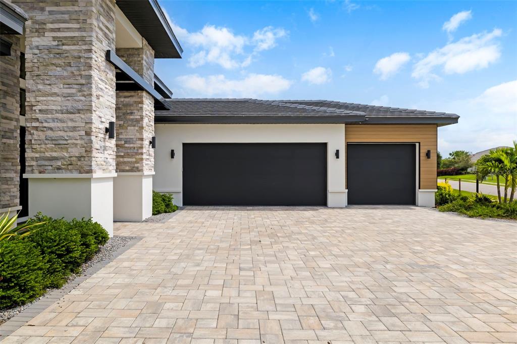 A modern house exterior features a stone pillar, two dark garage doors, and a paver driveway — 4116 BUTTE TRAIL, BRADENTON, FL