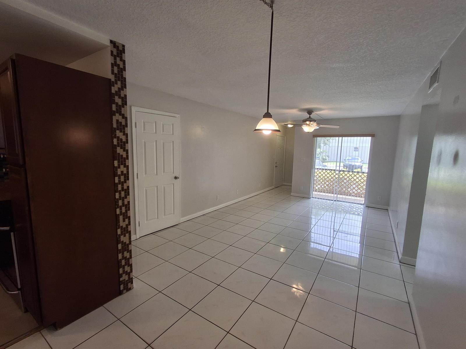 An open-concept dining area features white tile flooring, a pendant light, and a sliding door — 512 Gardens Drive # 103, Pompano Beach FL 33069, POMPANO BEACH, FL