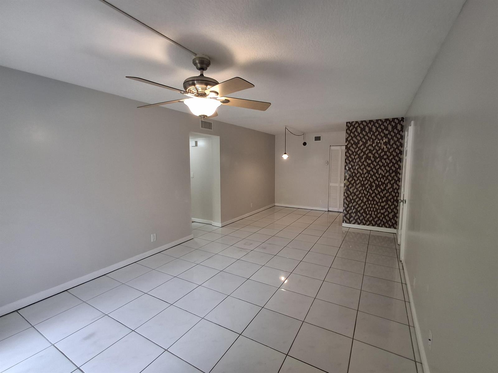 An empty room features white tile flooring, a ceiling fan, and a decorative accent wall — 512 Gardens Drive # 103, Pompano Beach FL 33069, POMPANO BEACH, FL