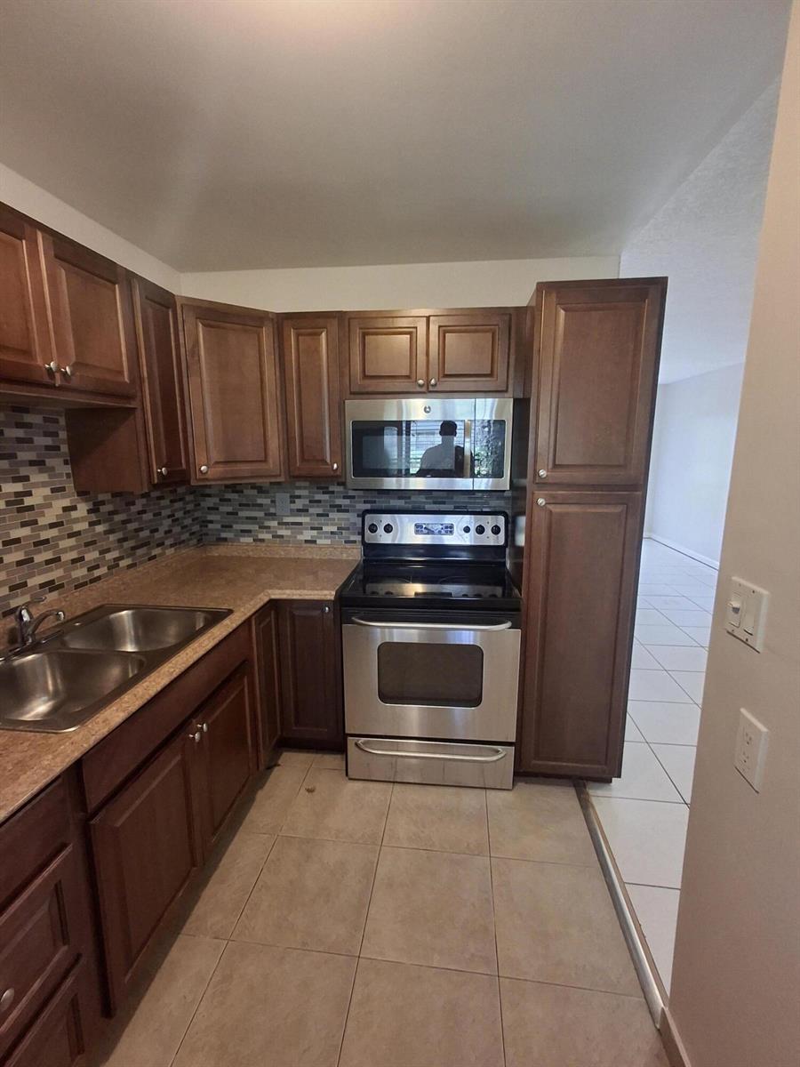 A kitchen features brown wooden cabinets, stainless steel appliances, a tiled backsplash, and tile flooring — 512 Gardens Drive # 103, Pompano Beach FL 33069, POMPANO BEACH, FL