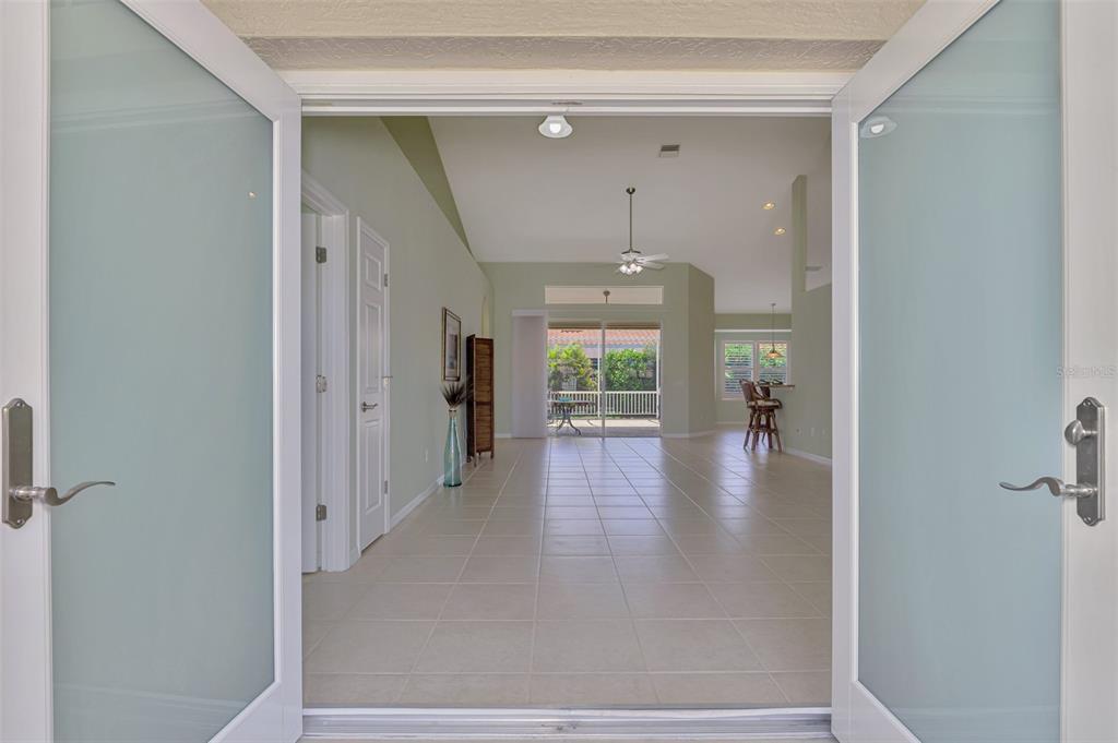 A view through open double doors into a tiled living area with a vaulted ceiling — 5879 MADISON ROAD, VENICE, FL