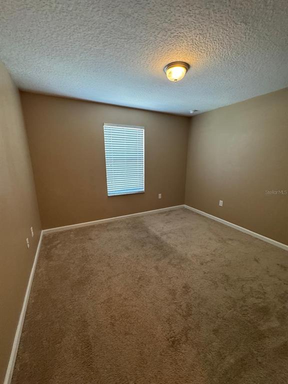 An empty bedroom with tan walls, beige carpeting, and a single window with white blinds — 1428 CHELSEA DRIVE, DAVENPORT, FL