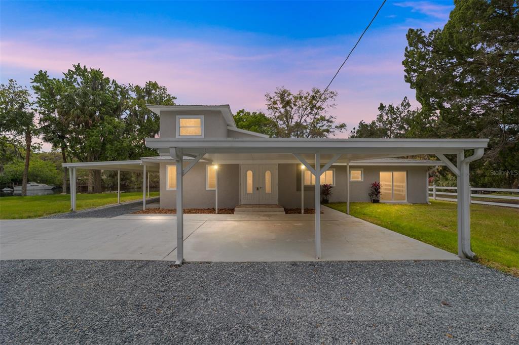 A gray two-story house features a large attached carport and a gravel driveway — 34 GARDEN MALL COURT, INGLIS, FL