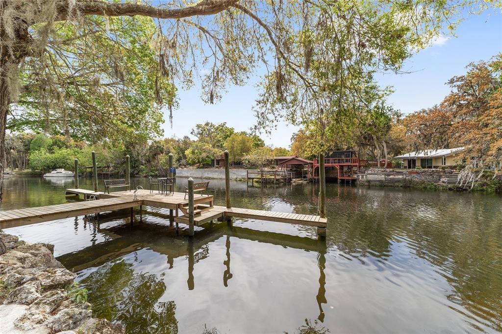 A wooden dock extends into a calm river surrounded by trees and waterfront homes — 34 GARDEN MALL COURT, INGLIS, FL