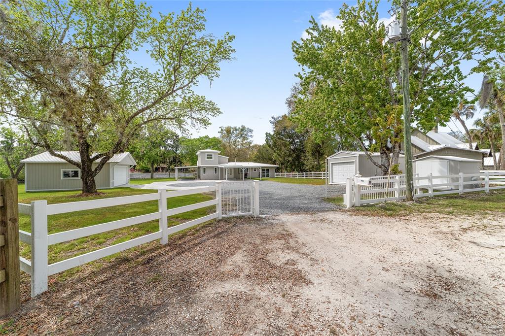 A gravel driveway leads to a house with two detached garages behind a white fence — 34 GARDEN MALL COURT, INGLIS, FL