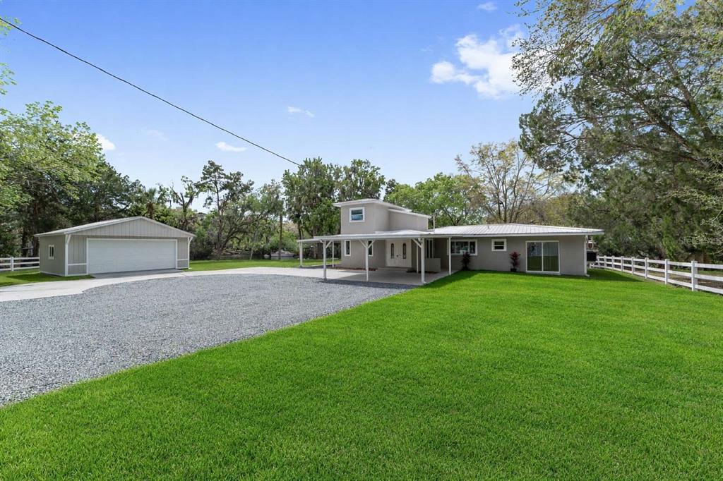 A light-colored house with a detached garage, a gravel driveway, and a white fence — 34 GARDEN MALL COURT, INGLIS, FL