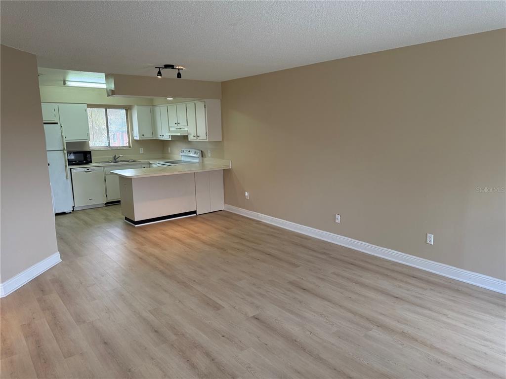 A kitchen with white cabinets and a breakfast bar opens into a spacious living area — 7340 SWALLOW RUN UNIT 7340, WINTER PARK, FL