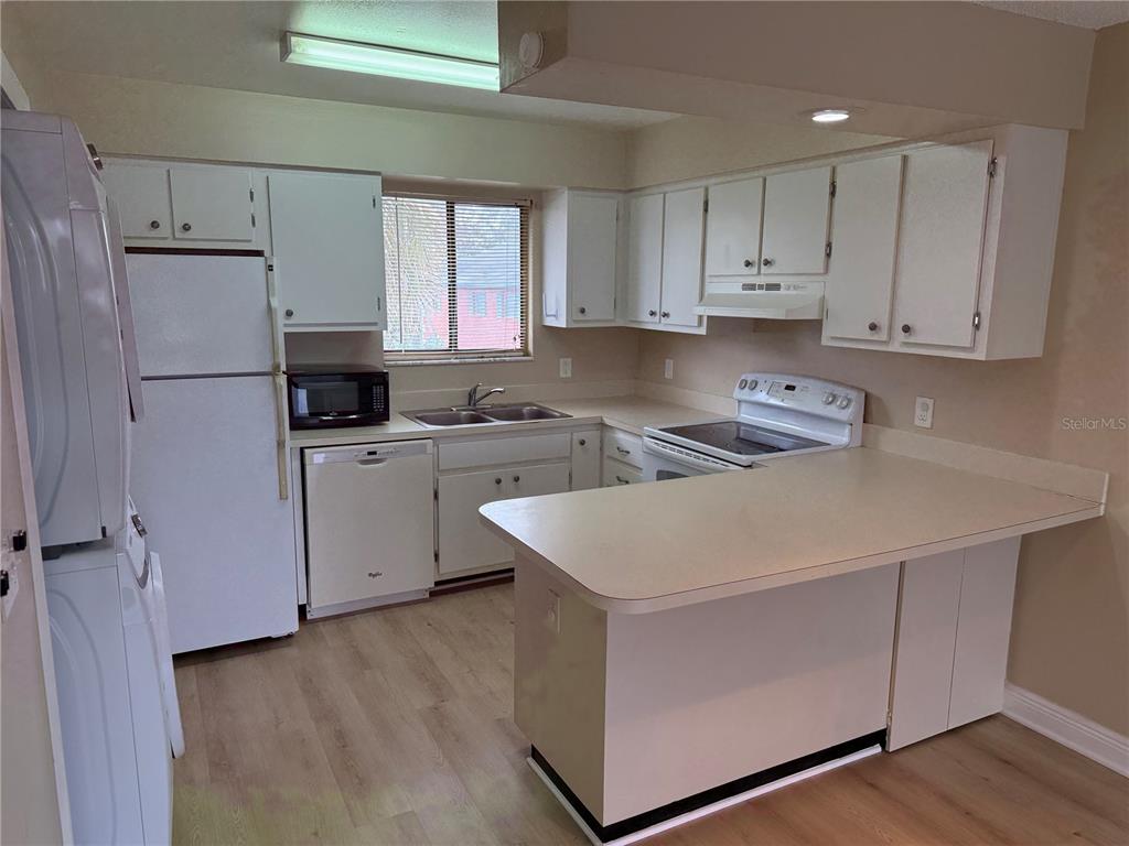 A kitchen features white cabinets, white appliances, a peninsula counter, and light wood-look flooring — 7340 SWALLOW RUN UNIT 7340, WINTER PARK, FL