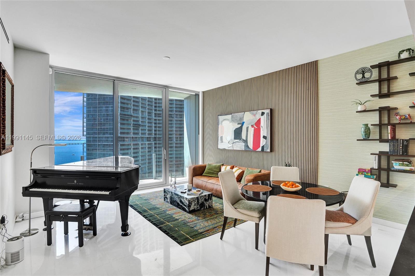 A modern living and dining room features a grand piano, leather sofa, and ocean views — 300 Biscayne Boulevard Way # 2106W, Miami FL 33131, MIAMI, FL