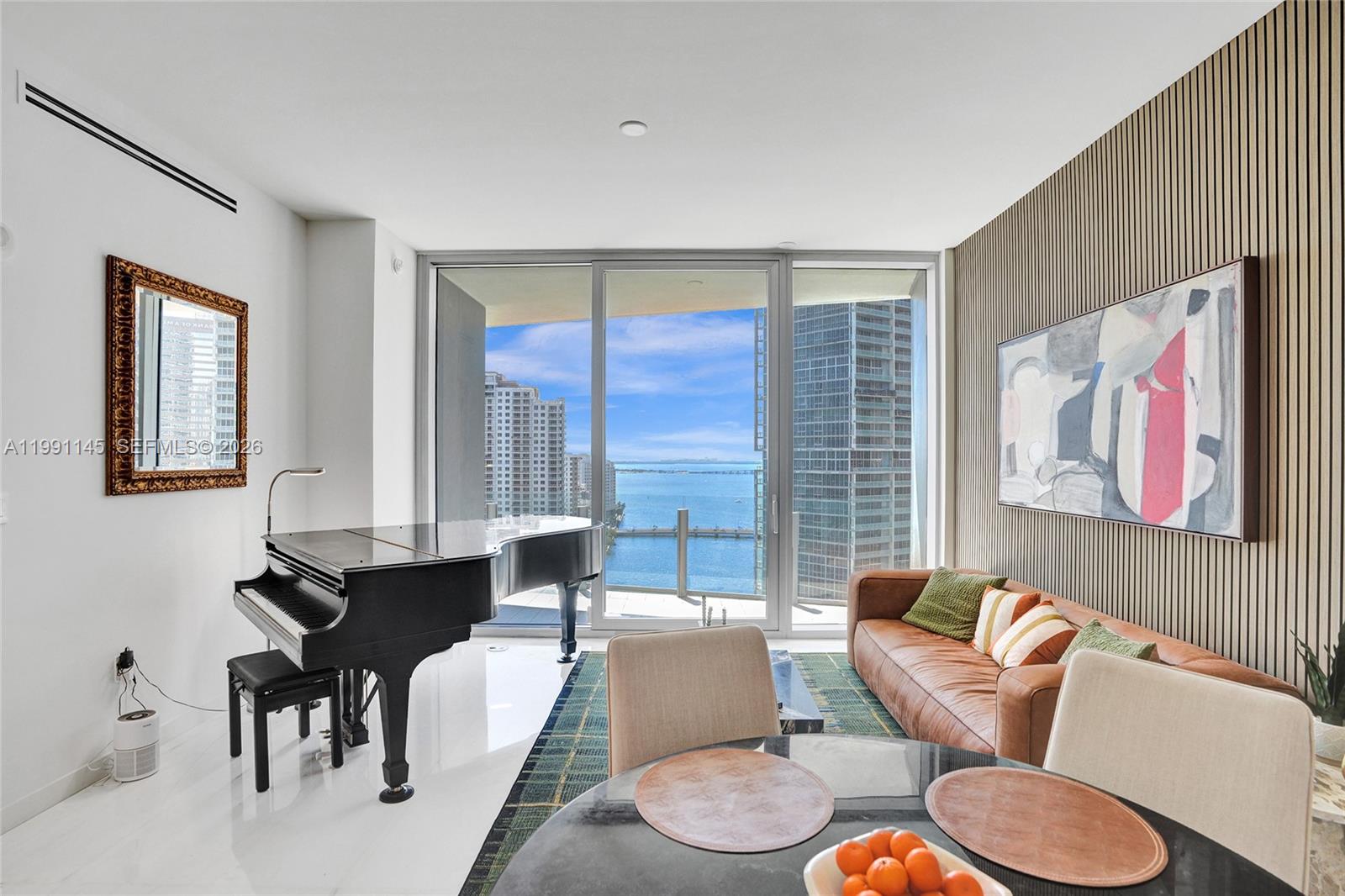 A living room features a grand piano, leather sofa, and floor-to-ceiling windows overlooking the ocean — 300 Biscayne Boulevard Way # 2106W, Miami FL 33131, MIAMI, FL
