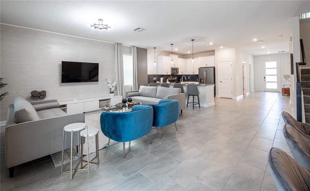 An open-concept living room and kitchen featuring gray tile flooring and blue accent chairs — 840 DROP SHOT DRIVE, DAVENPORT, FL