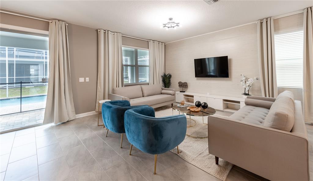 A living room features two beige sofas, two blue velvet chairs, and a wall-mounted television — 840 DROP SHOT DRIVE, DAVENPORT, FL