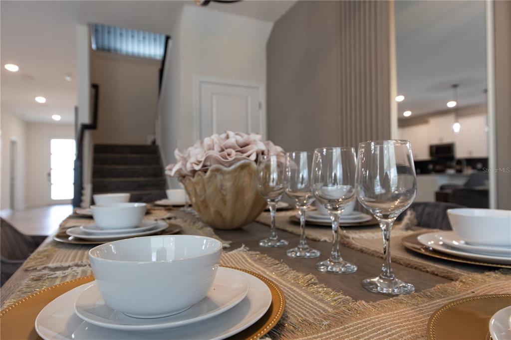 A dining table is set with white bowls, plates, and wine glasses in a home — 840 DROP SHOT DRIVE, DAVENPORT, FL
