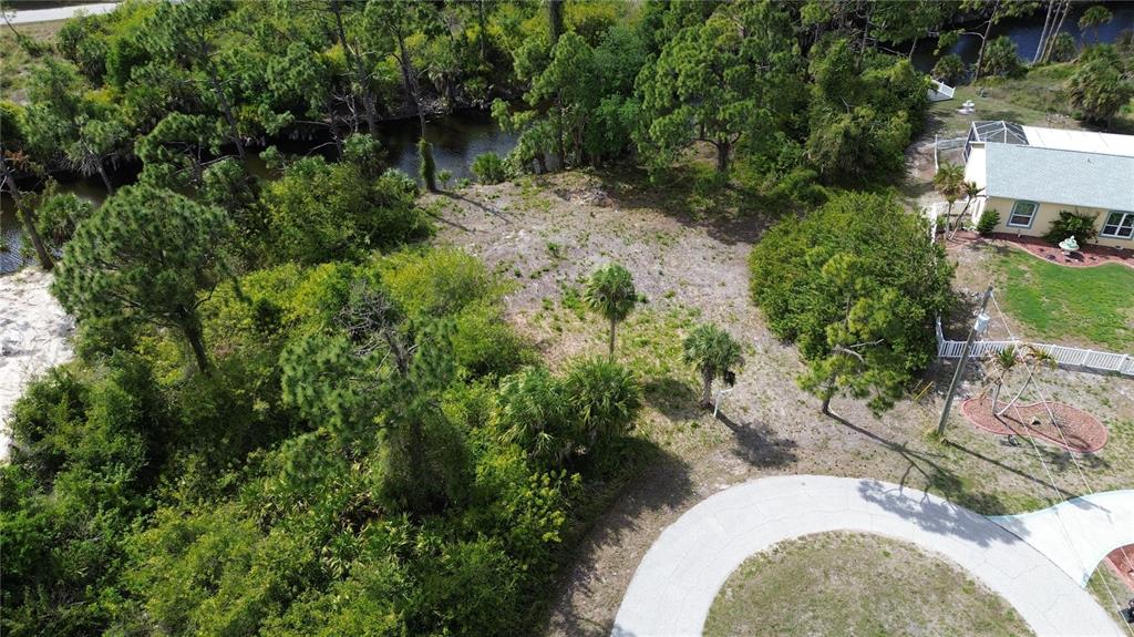 An aerial view shows a vacant, wooded lot adjacent to a house and a canal — 7711 COSMO COURT, PORT CHARLOTTE, FL