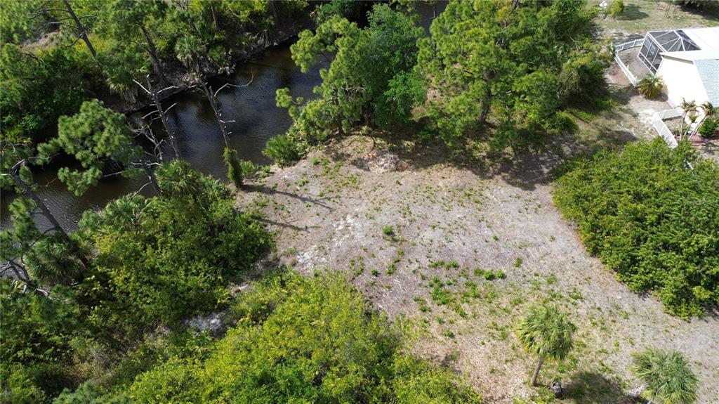 An aerial view shows a vacant, sandy lot bordered by a canal and dense vegetation — 7711 COSMO COURT, PORT CHARLOTTE, FL