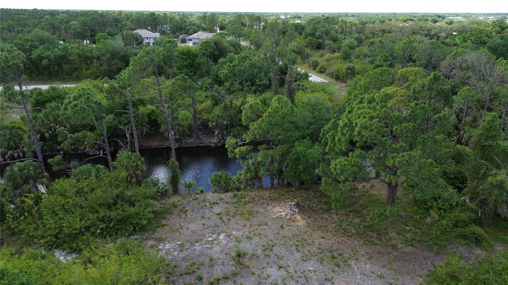 An aerial view of a vacant, wooded lot featuring a canal and surrounding residential homes — 7711 COSMO COURT, PORT CHARLOTTE, FL