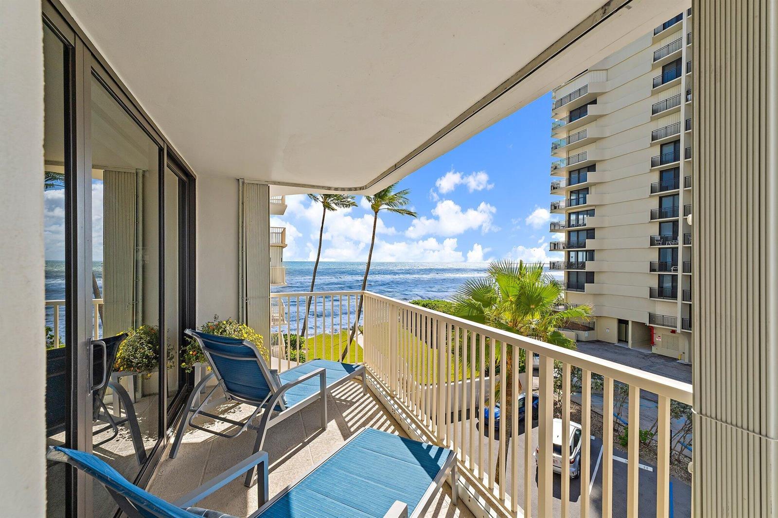 A balcony with blue lounge chairs overlooks the ocean and a neighboring high-rise building — 5480 N Ocean Drive, Singer Island FL 33404, SINGER ISLAND, FL