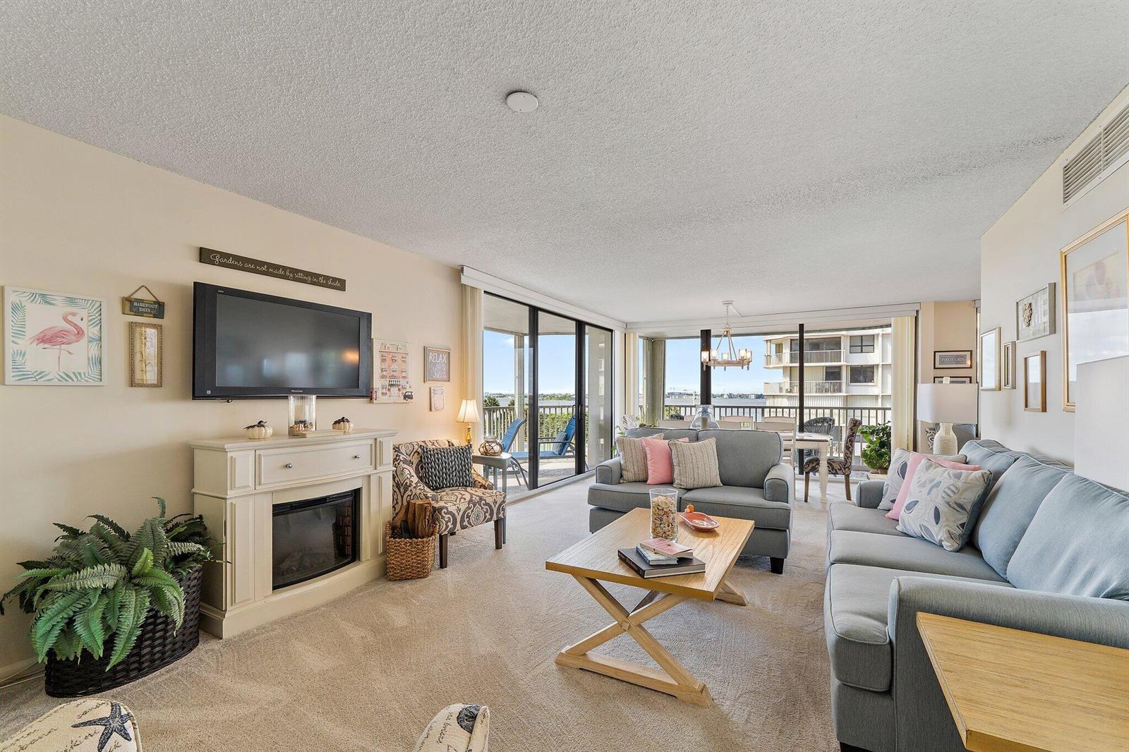 A living room features a fireplace, a television, two sofas, and a balcony with water views — 5480 N Ocean Drive, Singer Island FL 33404, SINGER ISLAND, FL
