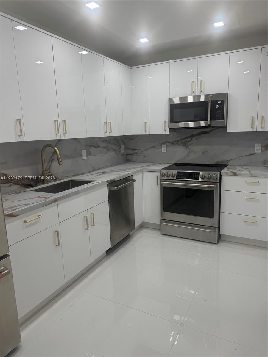 A modern kitchen features white glossy cabinets, stainless steel appliances, and marble-patterned countertops — 10185 Collins Ave # 606, Bal Harbour FL 33154, BAL HARBOUR, FL