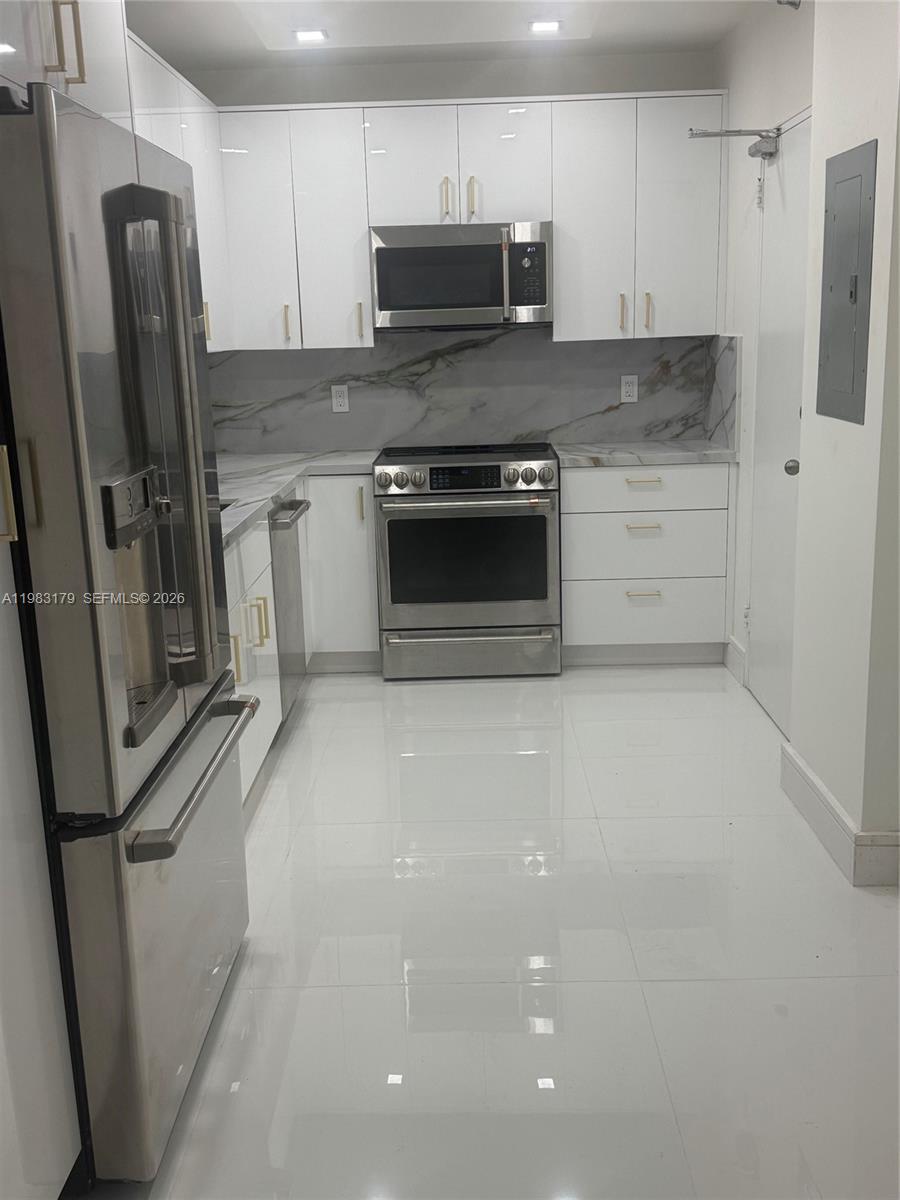 A modern kitchen features white glossy cabinets, stainless steel appliances, and marble-patterned countertops and backsplash — 10185 Collins Ave # 606, Bal Harbour FL 33154, BAL HARBOUR, FL