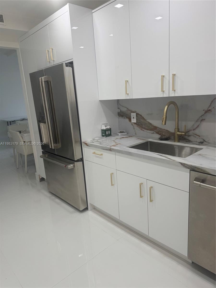 A modern kitchen features white glossy cabinets, stainless steel appliances, and white tile flooring — 10185 Collins Ave # 606, Bal Harbour FL 33154, BAL HARBOUR, FL