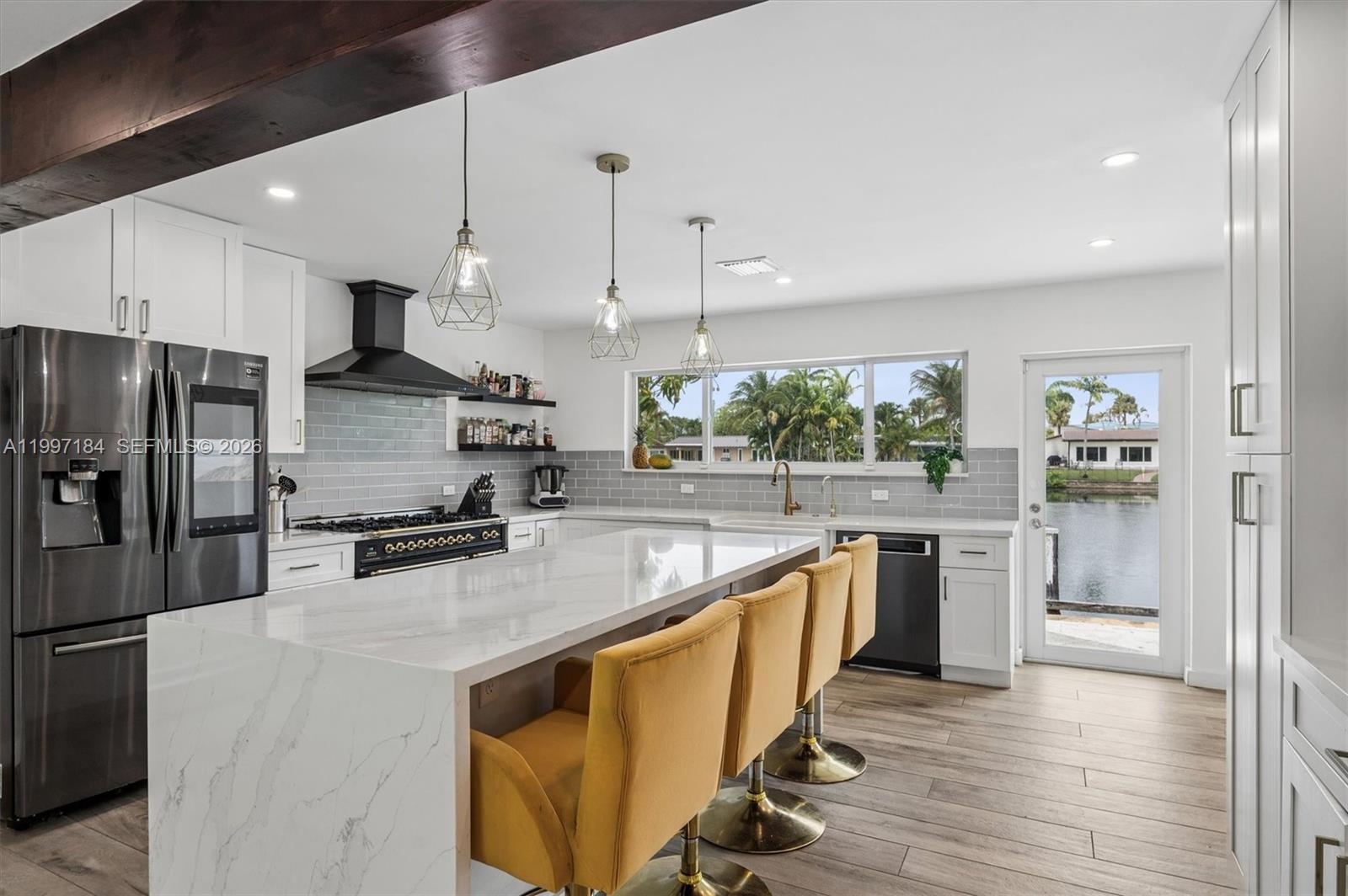 A modern kitchen features a marble waterfall island, yellow bar stools, and waterfront views — 717 NW 30th St, Wilton Manors FL 33311, WILTON MANORS, FL