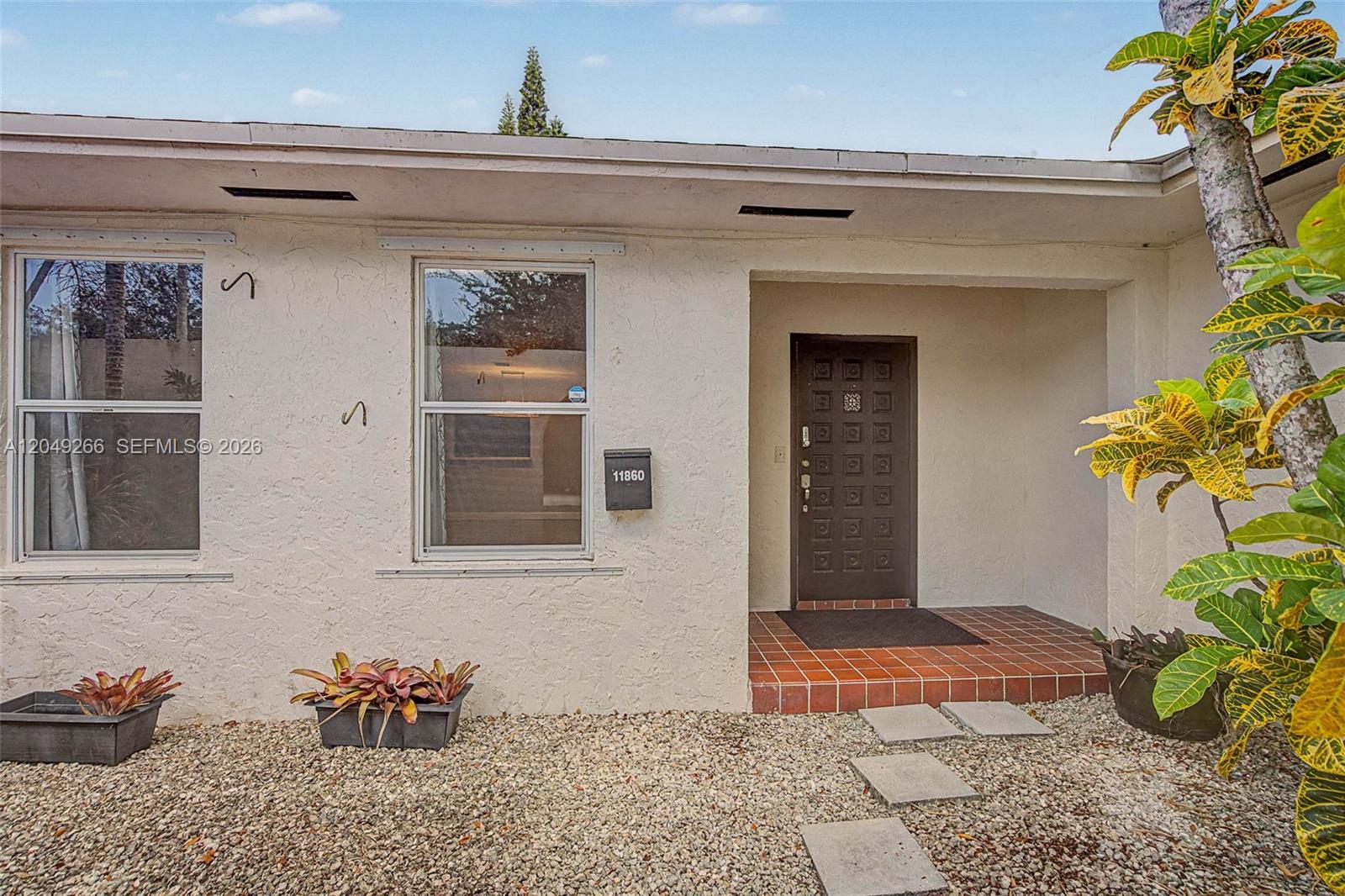 The exterior of a house features a brown front door, a gravel yard, and plants — 11860 SW 81st Rd # 11860, Pinecrest FL 33156, PINECREST, FL