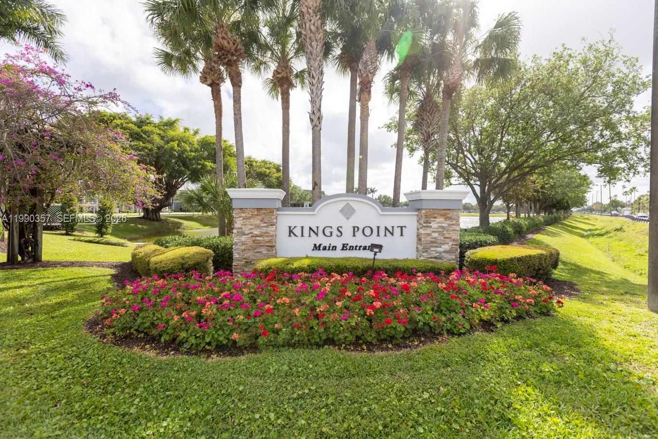 A stone monument sign for Kings Point stands in a landscaped garden with flowering plants — 294 Brittany G # 294, Delray Beach FL 33446, DELRAY BEACH, FL