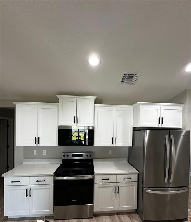 A kitchen features white cabinets, stainless steel appliances, and light-colored countertops — 1501 NW 4TH STREET, CAPE CORAL, FL