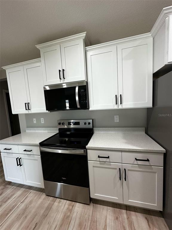 A kitchen features white shaker cabinets, a stainless steel stove, and light-colored speckled countertops — 1501 NW 4TH STREET, CAPE CORAL, FL