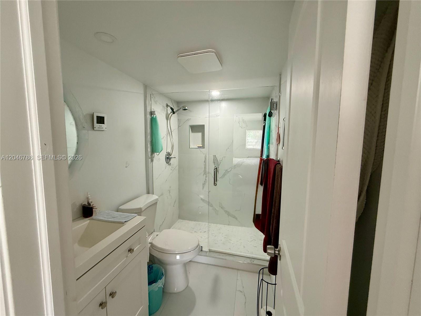A small bathroom features a white vanity, a toilet, and a glass-enclosed marble shower — 14790 Bonaire Blvd # 202, Delray Beach FL 33446, DELRAY BEACH, FL