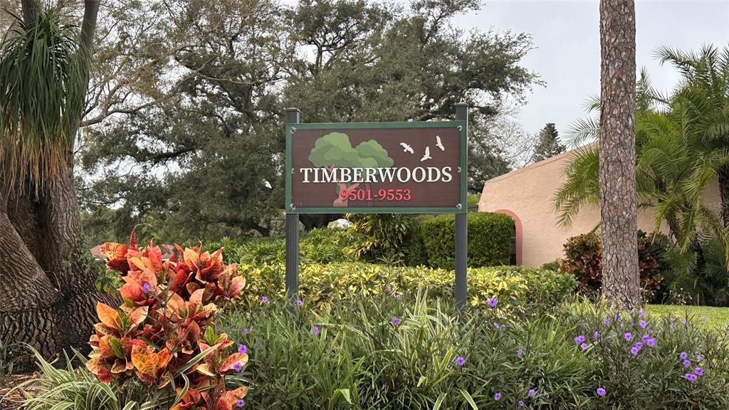 A sign for Timberwoods stands in front of a landscaped garden and a building — 9783 86TH AVENUE, SEMINOLE, FL