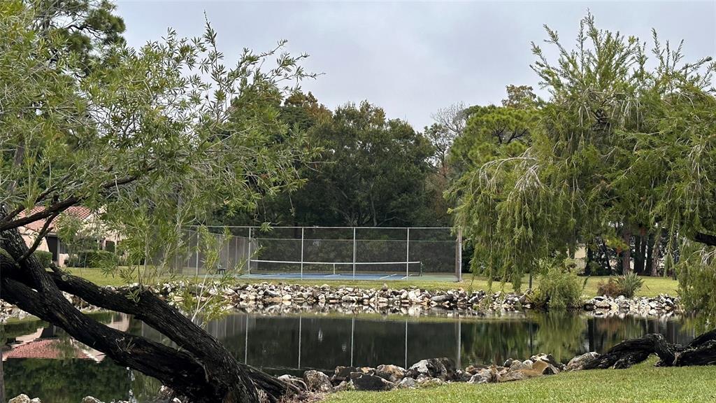A tennis court sits behind a small pond surrounded by trees and a rock border — 9783 86TH AVENUE, SEMINOLE, FL