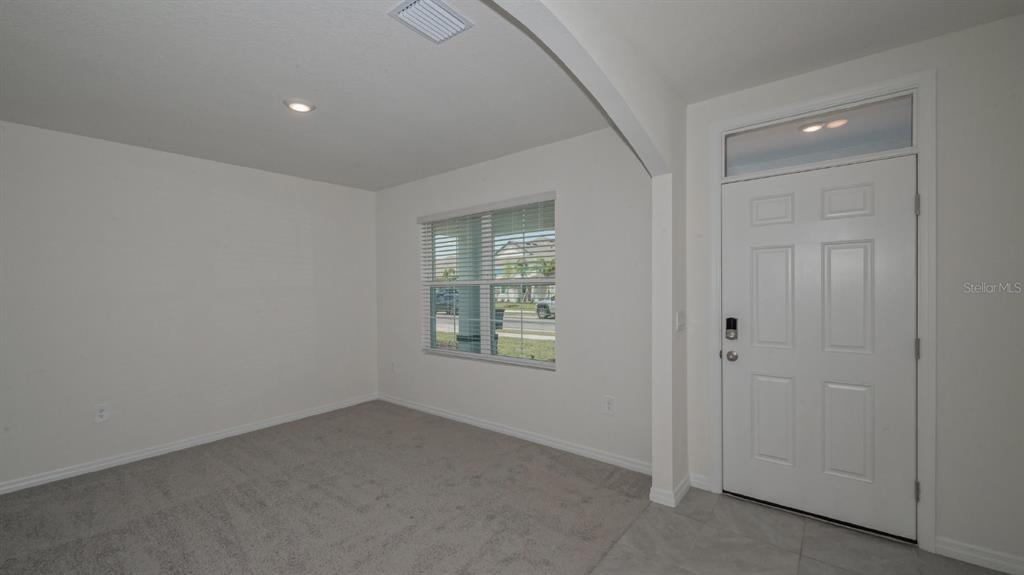 A carpeted room with a window and a white front door with a transom window — 5657 SOFT SKIES DRIVE, SARASOTA, FL