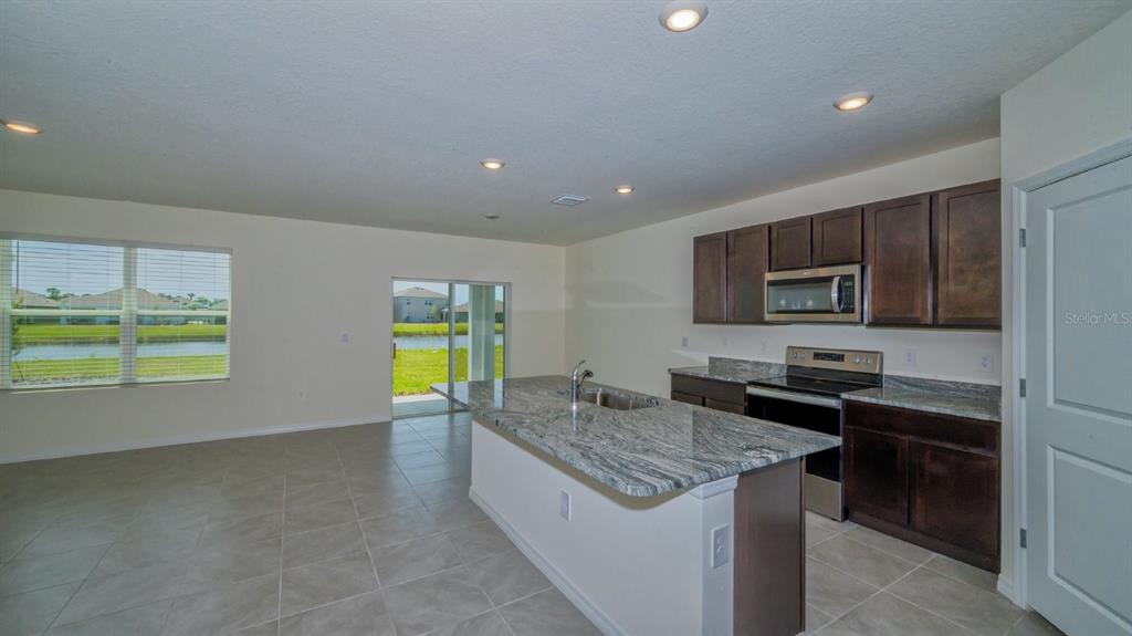 A kitchen with dark wood cabinets, granite countertops, and an island overlooks a backyard pond — 5657 SOFT SKIES DRIVE, SARASOTA, FL