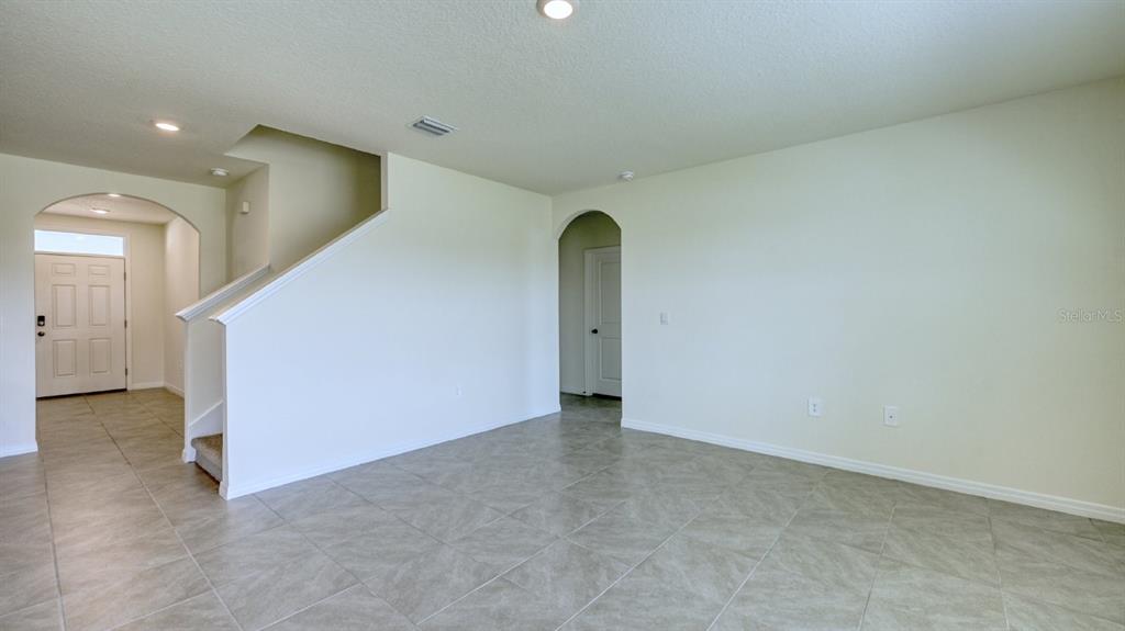 An empty living area features light-colored tile flooring, white walls, and an arched entryway — 5657 SOFT SKIES DRIVE, SARASOTA, FL