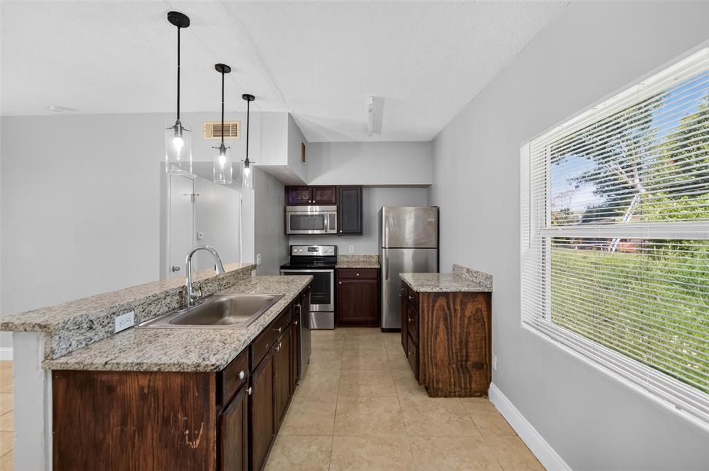 A kitchen features dark wood cabinets, granite countertops, stainless steel appliances, and three pendant lights — 4001 MONARCH DRIVE, ORLANDO, FL