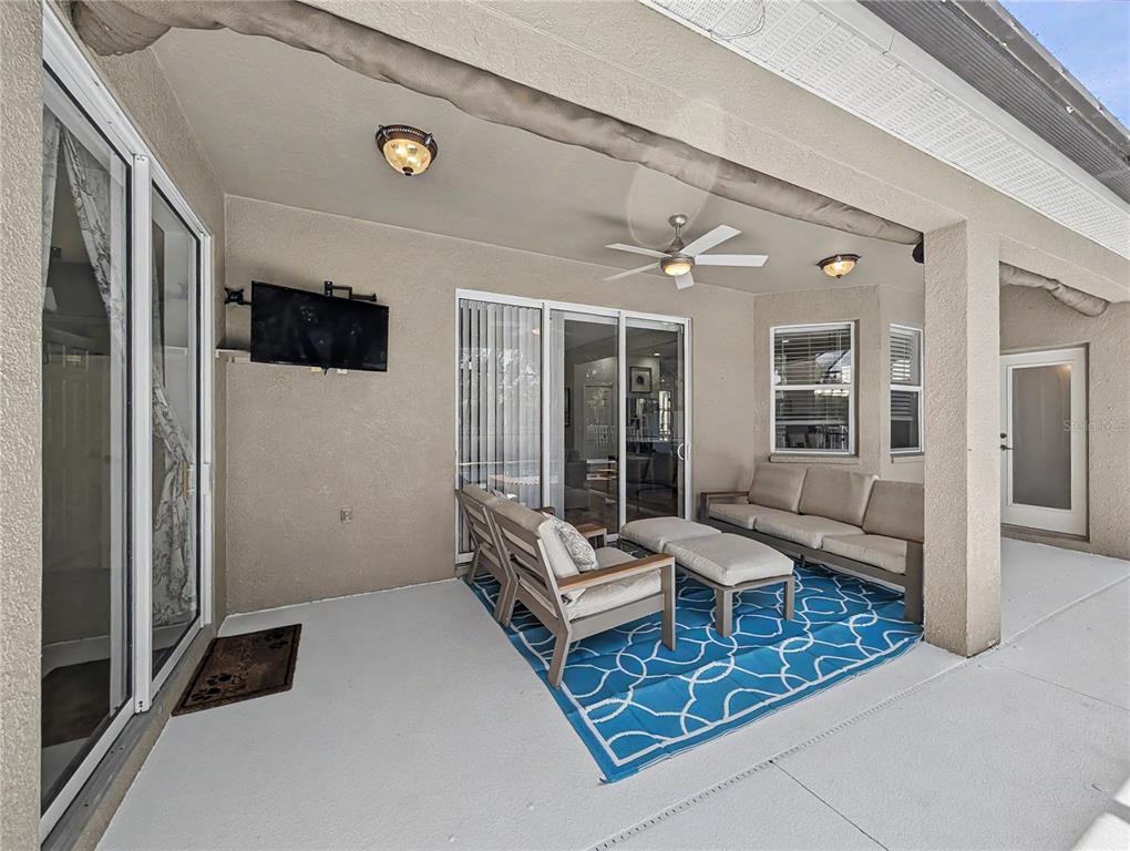 A covered patio features a seating area with outdoor furniture, a television, and ceiling fans — 4414 67TH AVENUE CIRCLE E, SARASOTA, FL