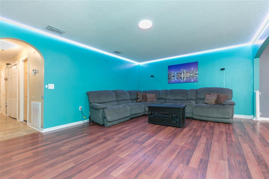 A living room features bright teal walls, LED cove lighting, a gray sectional, and wood-look flooring — 9922 ASHBURN LAKE DRIVE, TAMPA, FL
