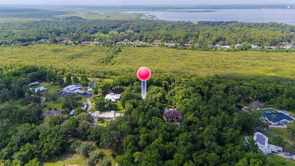 An aerial view shows a large house nestled in a dense forest near a lake — 325 STILLBROOK TRAIL, DELTONA, FL