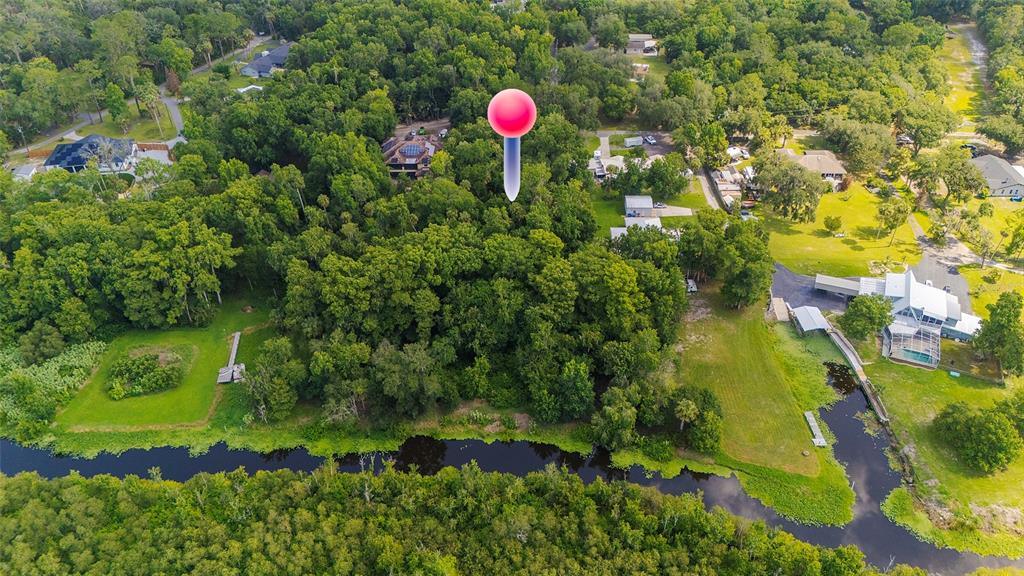 An aerial view shows a wooded lot with a pink location pin near a canal — 325 STILLBROOK TRAIL, DELTONA, FL