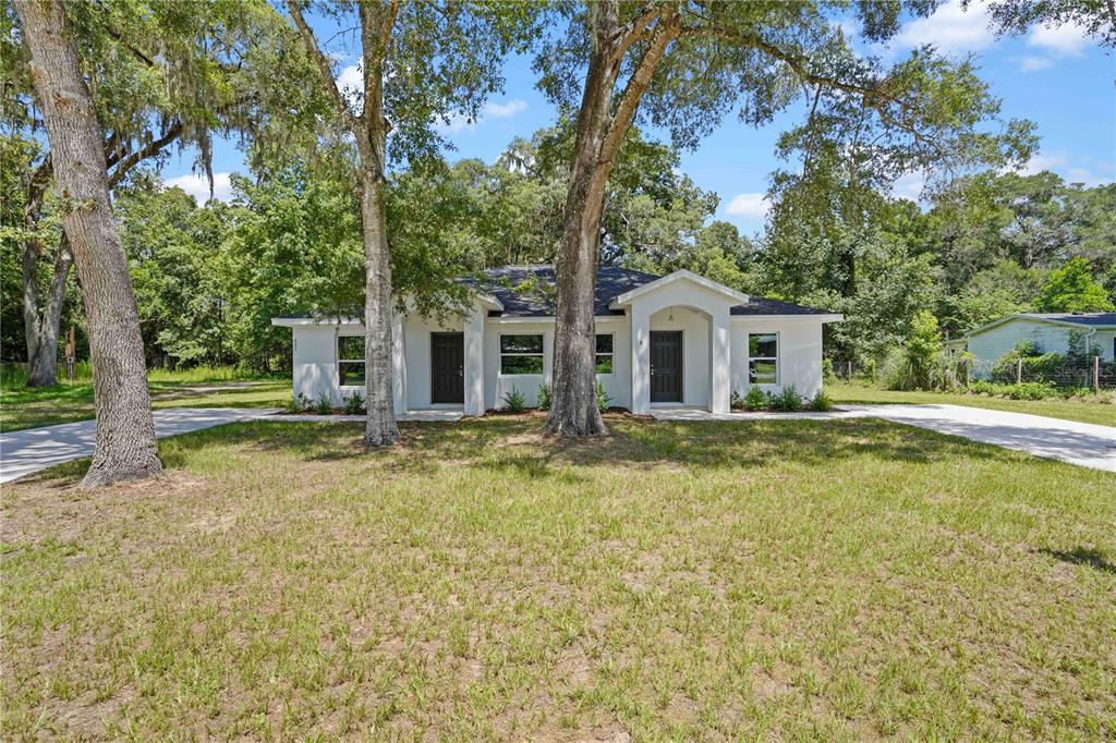 A single-story white duplex with two front doors sits on a grassy lot with trees — 607 SE 4TH DRIVE UNIT A & B, WILLISTON, FL