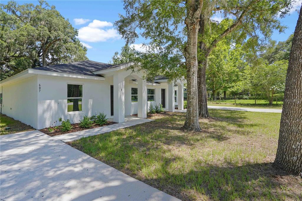A white, single-story duplex with a concrete driveway and mature trees in the front yard — 607 SE 4TH DRIVE UNIT A & B, WILLISTON, FL