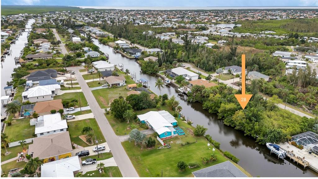 An aerial view shows a canal-front residential neighborhood with a vacant lot marked by an arrow — 3410 COLONY COURT, PUNTA GORDA, FL