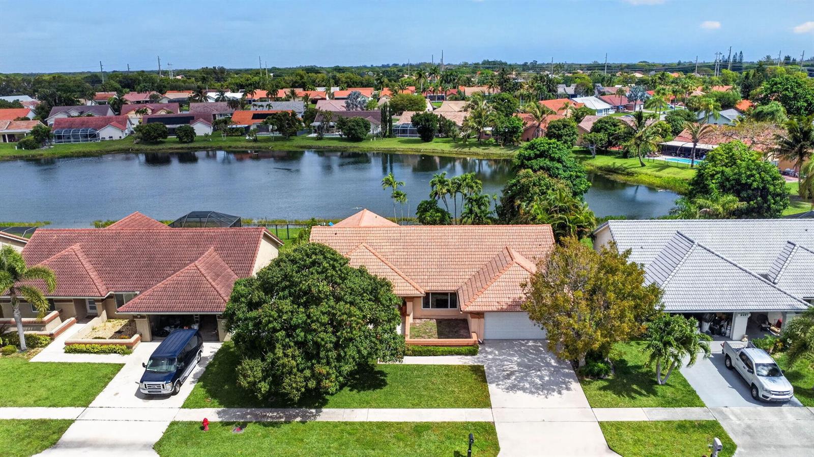 An aerial view shows three suburban houses with tiled roofs situated along a lake — 9501 Majestic Way, Boynton Beach FL 33437, BOYNTON BEACH, FL
