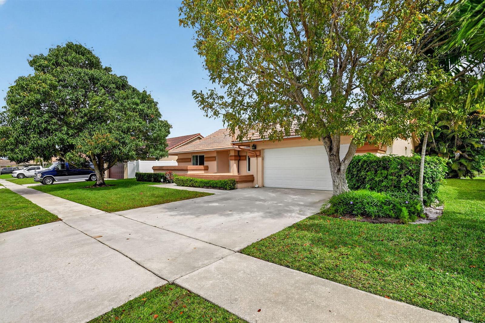 A single-story house with a white garage door, concrete driveway, and large trees in front — 9501 Majestic Way, Boynton Beach FL 33437, BOYNTON BEACH, FL