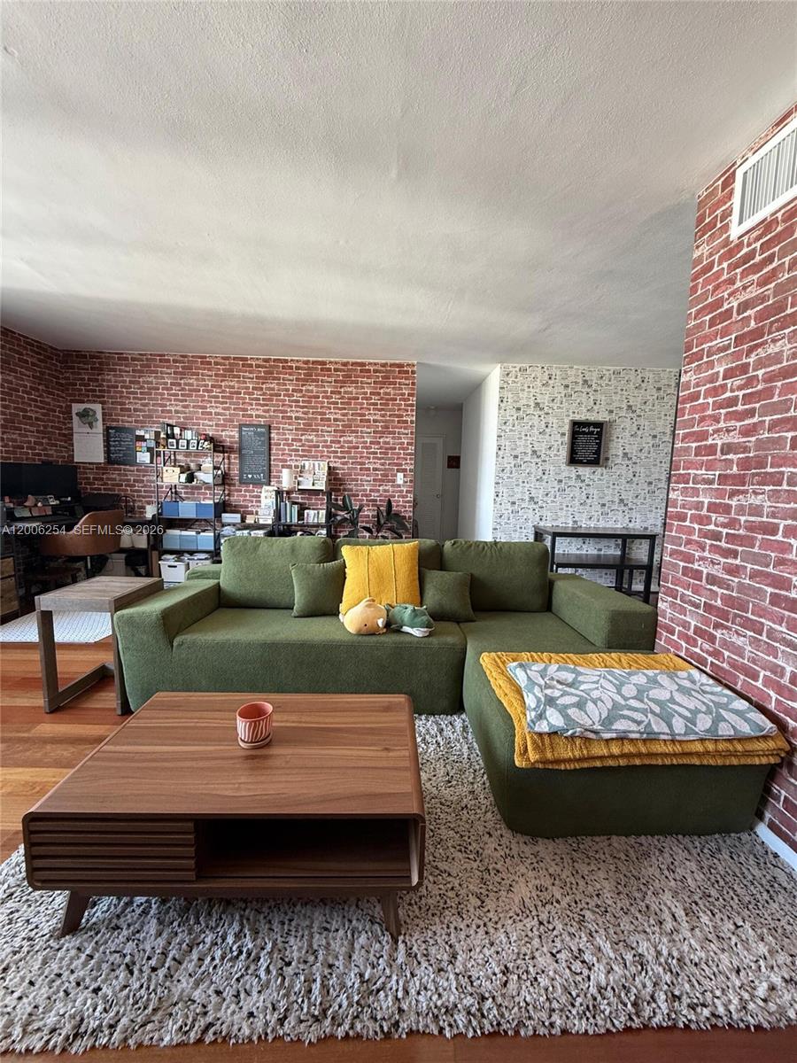 A living room features a green sectional sofa, a wooden coffee table, and brick-patterned wallpaper — 1000 West Ave # 1105, Miami Beach FL 33139, MIAMI BEACH, FL
