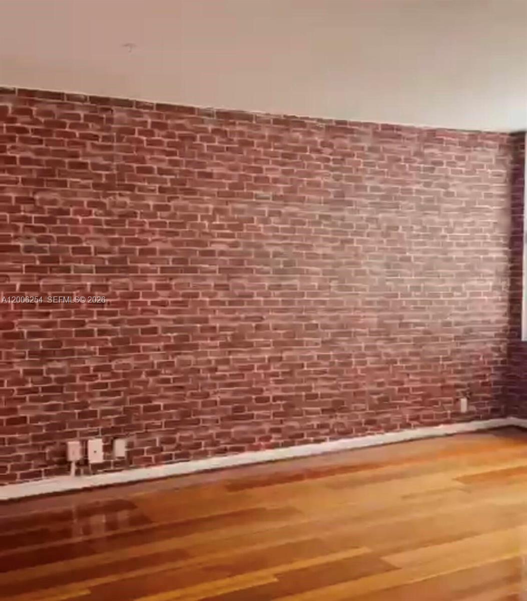 An empty room features a red faux-brick accent wall and hardwood flooring — 1000 West Ave # 1105, Miami Beach FL 33139, MIAMI BEACH, FL