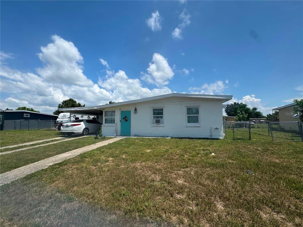 A white single-story house features a turquoise front door, a carport, and a grassy yard — 21472 MALLORY AVENUE, PORT CHARLOTTE, FL